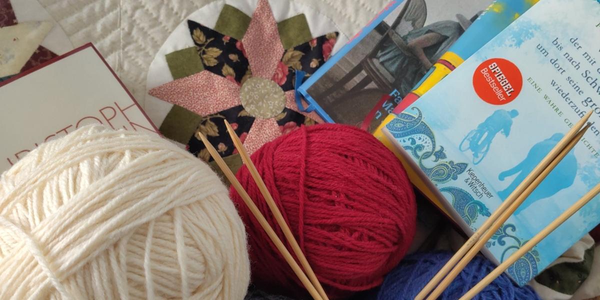 Bücher, Wolle und Stricknadeln auf einer Quiltdecke