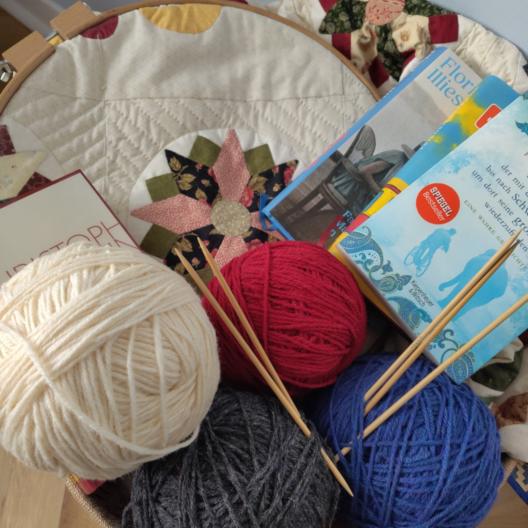 Bücher, Wolle und Stricknadeln auf einer Quiltdecke